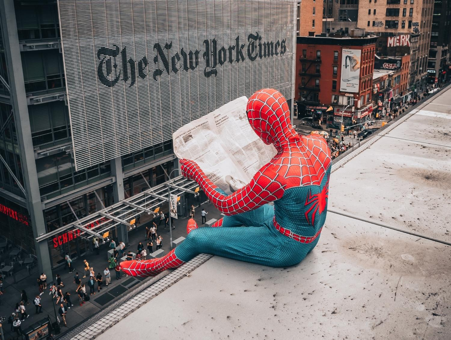 a young man dressed as spider man sitting on a ledge reading the local newspaper about a buy local e-commerce marketplace website